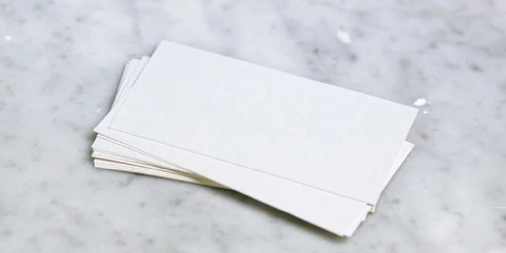 A small stack of blank white business cards is fanned out on a light gray marble surface, much like a precise setup of perfectly aligned paper towels. The cards are neatly arranged, with their edges aligned.